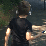 Photo of young boy walking and listening to music through headphones