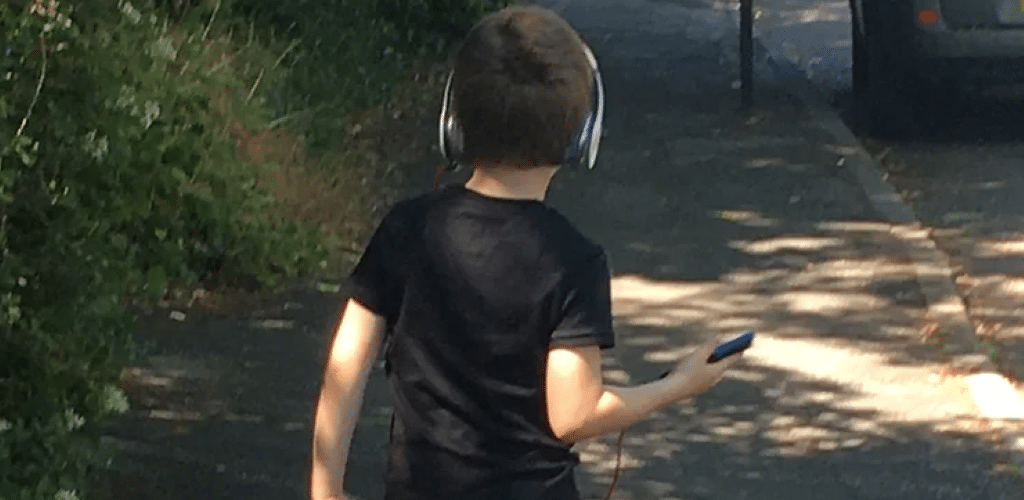 Photo of young boy walking and listening to music through headphones