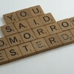 Photo of Scrabble game pieces on a white surface, ordered so they spell out 'You said tomorrow yesterday'.